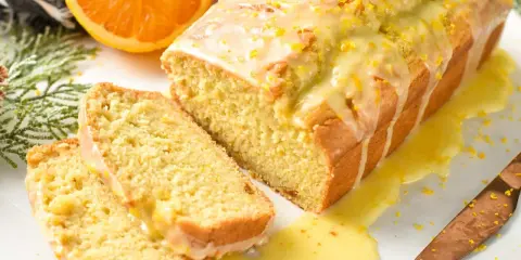 Un delicioso bizcocho de naranja, cubierto con glaseado y ralladura, con dos rebanadas cortadas.