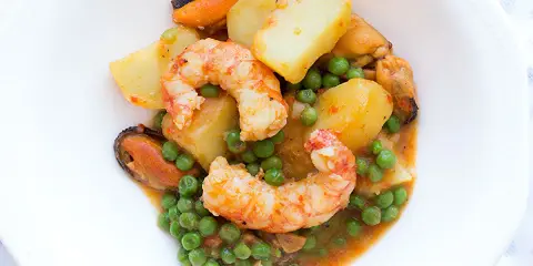 Patatas a la marinera con gambas, mejillones y guisantes en una salsa sabrosa.