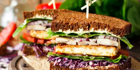 Delicioso sandwich vegetal con pan integral, tofu a la plancha, lechuga, tomate, cebolla morada y col lombarda.
