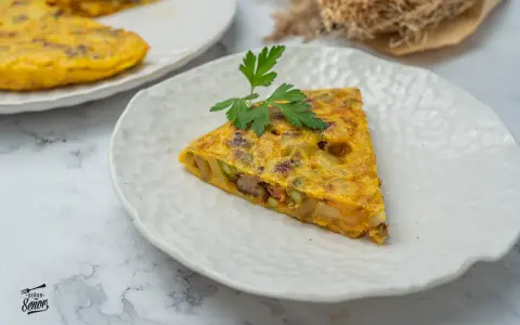 Un trozo de tortilla paisana, con patatas, verduras y chorizo, servida en un plato blanco texturizado.