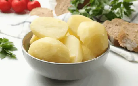 Un tazón lleno de patatas recién cocidas, listas para acompañar un pan rústico y tomates.