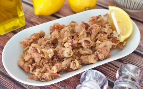 Crujientes puntillas de calamar fritas en un plato blanco, acompañadas de limón y aceite de oliva.
