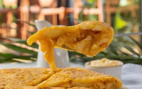 Un tenedor levanta un trozo de tortilla de patatas jugosa, mostrando su interior tierno y dorado.