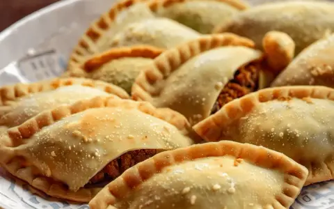 Empanadas doradas y crujientes, algunas con relleno visible de pechuga empanada, espolvoreadas con algo de sal.