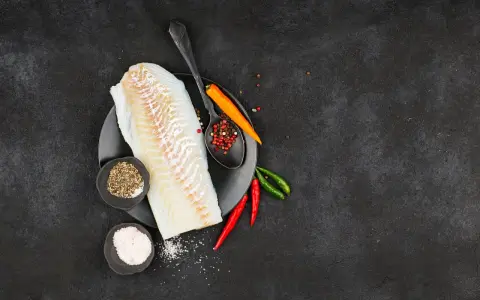 Filete de bacalao fresco listo para preparar a la brasa, con pimienta, sal y chiles.