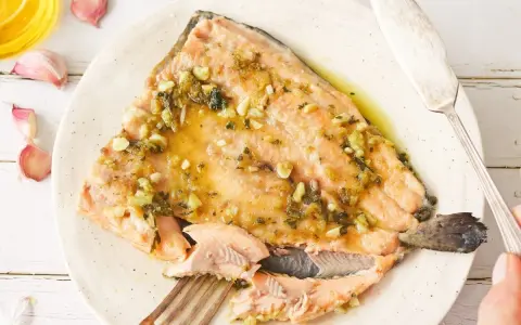 Deliciosa trucha al ajillo servida en un plato, con ajos y aceite de oliva alrededor.