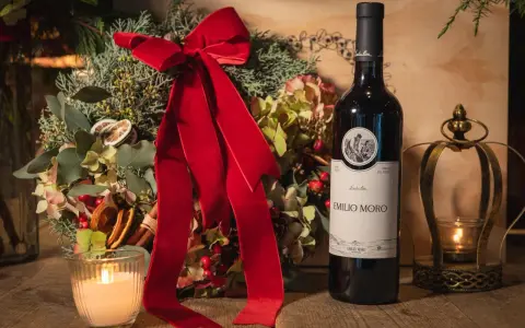 Botella de vino tinto fino Emilio Moro junto a un arreglo floral navideño, vela encendida y un candelabro dorado.