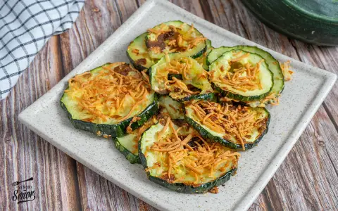 Rodajas de calabacín en freidora de aire, doradas y crujientes, con un toque de queso rallado. ¡Un snack saludable y delicioso!