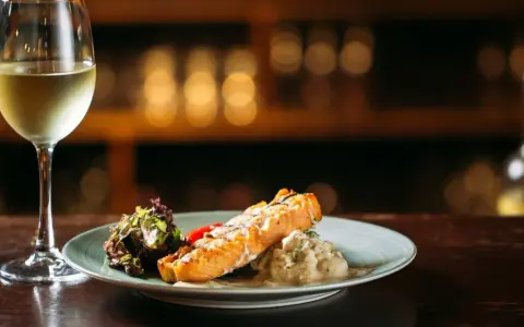 Un filete de salmón a la parrilla con ensalada y una copa de vino blanco, perfecto para un maridaje con riesling.