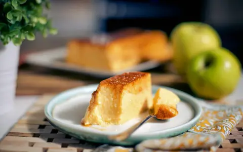 Un delicioso flan de manzana, con una porción servida en un plato, acompañado de manzanas verdes y una planta decorativa.