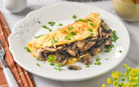 Tortilla de champiñones, dorada y esponjosa, rellena de sabrosos champiñones salteados y espolvoreada con perejil fresco.