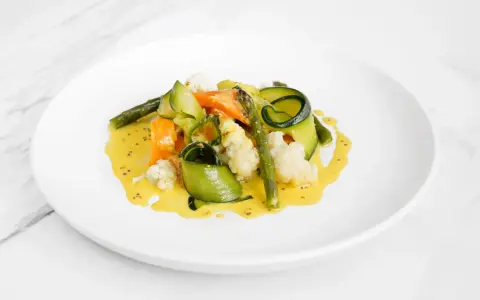 Deliciosas verduras al vapor, como zanahoria, calabacín en espiral, espárragos y coliflor, bañadas en una cremosa salsa amarilla.