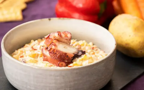 Deliciosa ensaladilla de pulpo cremosa, servida en cuenco, con patata, pimiento y zanahoria de fondo.