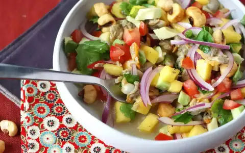 Un refrescante ceviche de berberechos con trozos de mango, aguacate, tomate y cebolla morada, servido en un cuenco blanco.