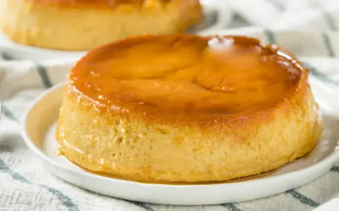 Delicioso flan de plátano con caramelo dorado, servido en un plato blanco sobre un mantel a rayas.