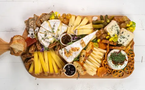 Una tabla de quesos sencilla con variedad de quesos, pan, frutas secas, uvas, pepinillos y mermelada.