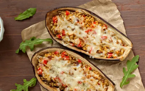 Dos mitades de berenjenas rellenas con cuscús, pimientos y queso derretido, cocinadas en airfryer.