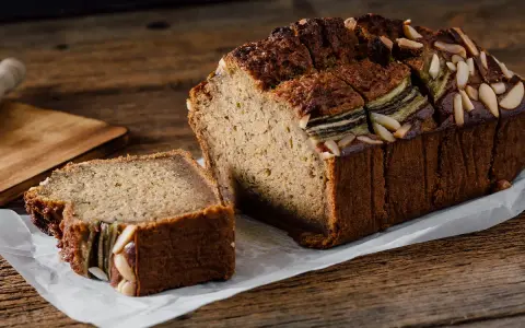 Un delicioso bizcocho de plátano, recién horneado y decorado con almendras laminadas, listo para disfrutar.
