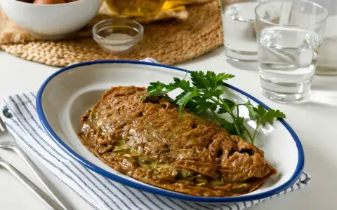 Tortilla de alcachofas dorada y jugosa, servida en plato blanco con borde azul. Decorada con perejil fresco.