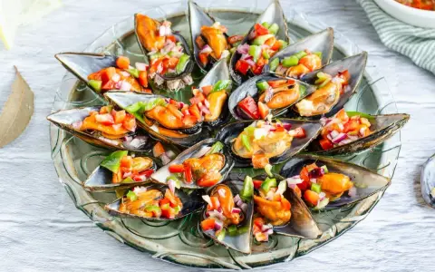 Mejillones a la vinagreta servidos en una bandeja de cristal, adornados con una colorida mezcla de pimientos y cebolla.