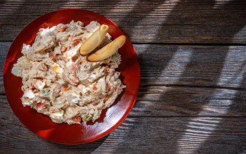 Ensaladilla rusa cremosa en plato rojo, con palitos de pan. ¿Cuanto dura la ensaladilla rusa en la nevera?