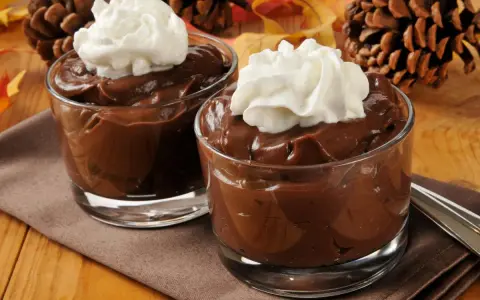 Dos copas de cremosas natillas de chocolate con nata montada, decoradas con piñas y hojas de otoño.