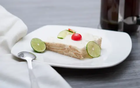 Deliciosa carlota de limón, con galletas y crema, decorada con rodajas de lima y una cereza.
