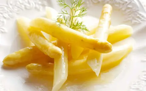 Espárragos blancos tiernos, listos para cocinar, servidos en un plato blanco con una ramita de eneldo.