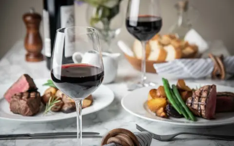 Dos copas de vino tinto, filetes jugosos y patatas asadas, perfectos para una cena de vino de invierno.