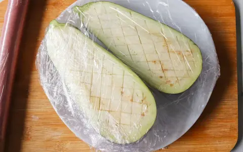 Dos mitades de berenjena cortadas en cubos y cubiertas con plástico, listas para cocinar berenjenas al microondas.