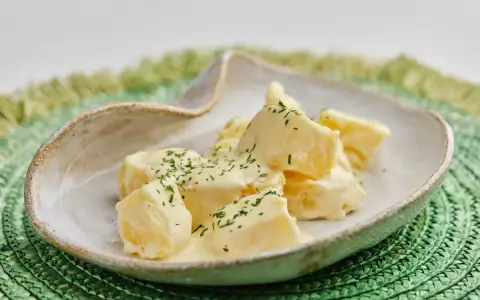 Patatas alioli cremosas y deliciosas, cubiertas con perejil fresco picado, servidas en un cuenco rústico sobre un salvamanteles verde.