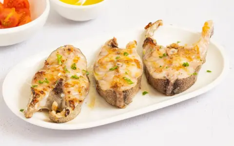 Tres rodajas de mero a la plancha, doradas y con perejil picado, servidas en plato blanco.