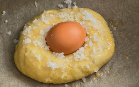 Masa para receta mona de pascua esponjosa, con un huevo crudo incrustado y espolvoreada con azúcar.