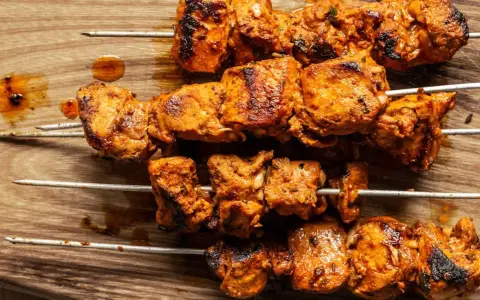 Cuatro brochetas de pinchos morunos auténticos, jugosos y dorados, sobre una tabla de madera.