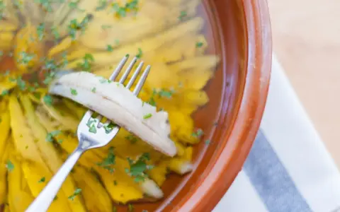 Boquerones en vinagre, la receta de la abuela, listos para disfrutar. Un tenedor recoge un boquerón marinado en aceite y vinagre, espolvoreado con perejil.