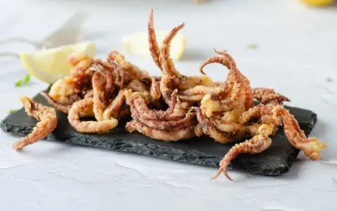 Crujientes rejos fritos servidos sobre pizarra negra, acompañados de gajos de limón.