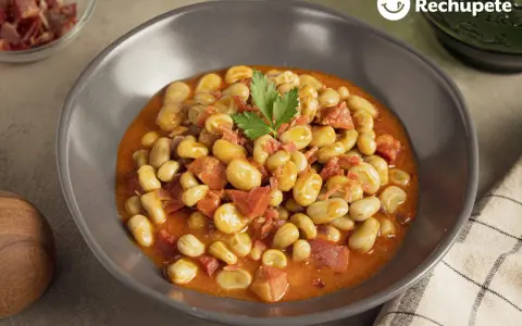 Plato de habas con jamón, guisadas en una salsa rojiza y decoradas con perejil.