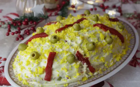 Ensaladilla rusa, la receta de la abuela, cubierta de mayonesa, huevo rallado, aceitunas y pimientos. ¡Un clásico festivo!