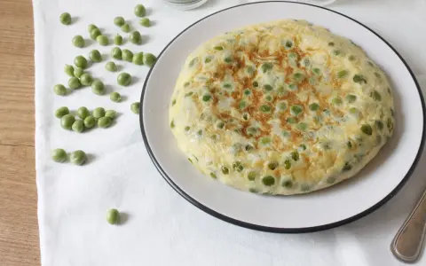 Tortilla de guisantes recién hecha, dorada y esponjosa, con guisantes verdes esparcidos por encima.