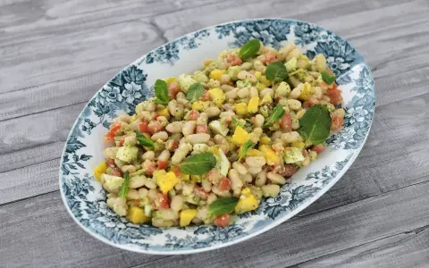 Deliciosa ensalada de alubias con trozos de tomate, mango y huevo, decorada con hojas de menta fresca.