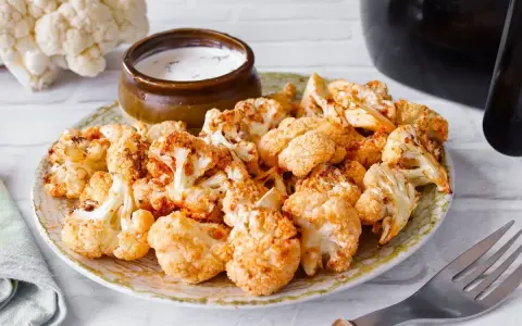 Coliflor airfryer dorada y crujiente servida en un plato con un tazón de salsa.
