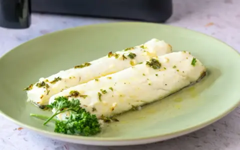 Dos filetes de merluza jugosos, recién salidos de la airfryer, con hierbas frescas y aceite de oliva.