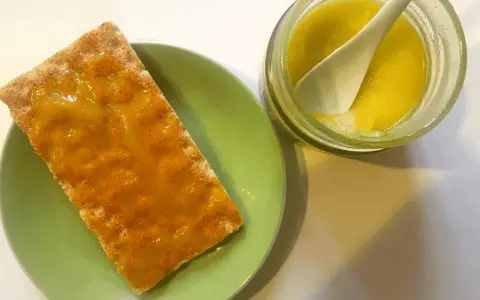 Galleta con mermelada de aceite de oliva, servida en plato verde junto a un tarro con la mermelada y una cuchara.