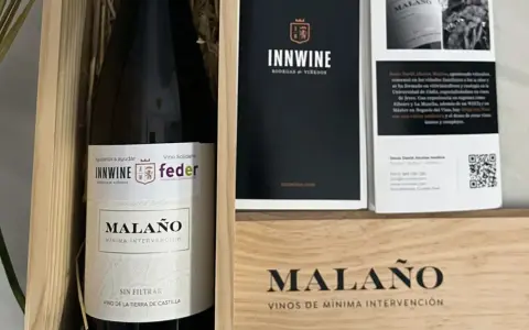 Caja de vino "Malaño" con etiqueta "Vino Solidario" y logos de INNWINE y feder. Incluye folleto informativo.