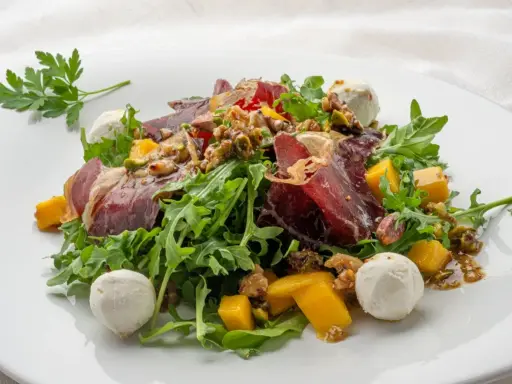 Deliciosa ensalada de cecina con mango, queso de cabra y nueces sobre rúcula fresca.