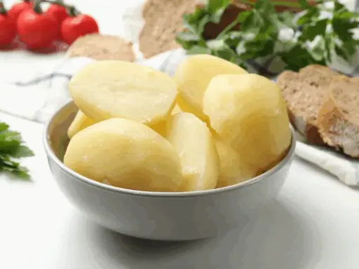 Un tazón lleno de patatas recién cocidas, listas para acompañar un pan rústico y tomates.