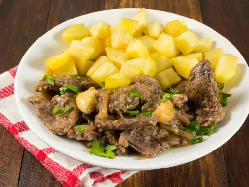 Plato de higaditos de pollo en salsa con patatas fritas en cubos, decorado con perejil fresco.