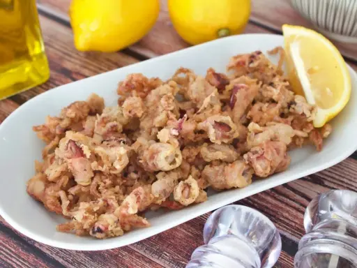 Crujientes puntillas de calamar fritas en un plato blanco, acompañadas de limón y aceite de oliva.