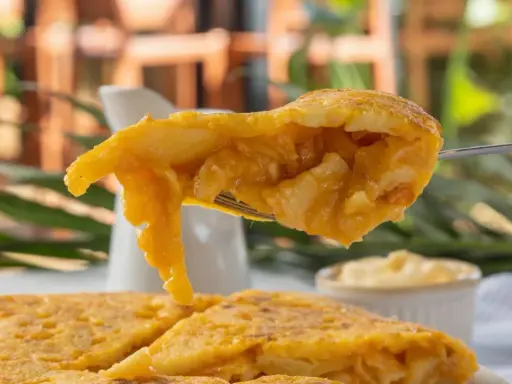 Un tenedor levanta un trozo de tortilla de patatas jugosa, mostrando su interior tierno y dorado.
