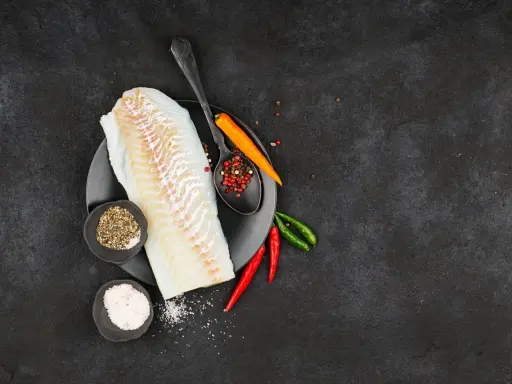 Filete de bacalao fresco listo para preparar a la brasa, con pimienta, sal y chiles.